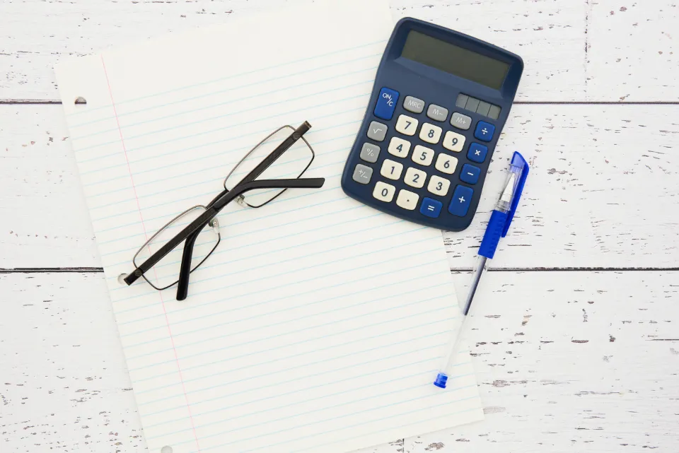 A calculator, a pen and reading glasses on a lined notepad