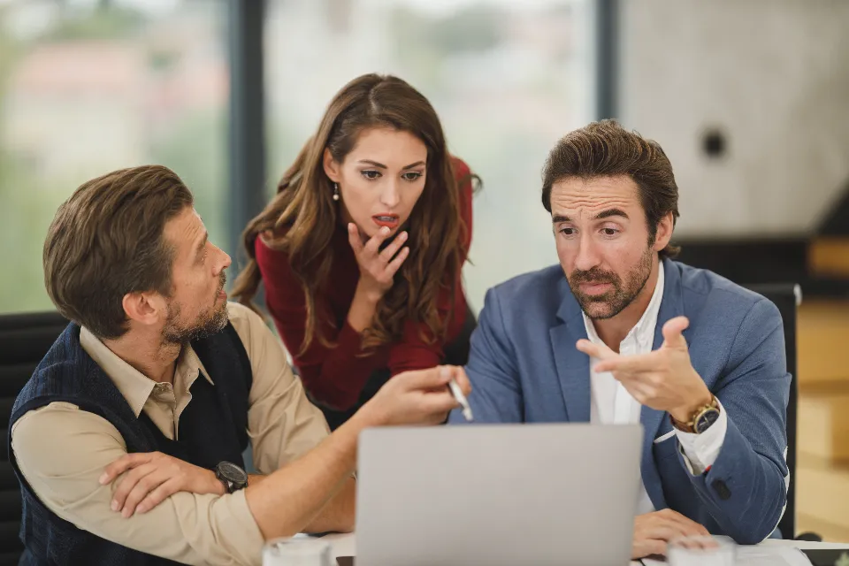 Three colleagues lean over a laptop together in a meeting